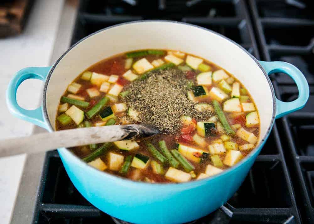 Adding spices into pot of minestrone soup on the stove. 