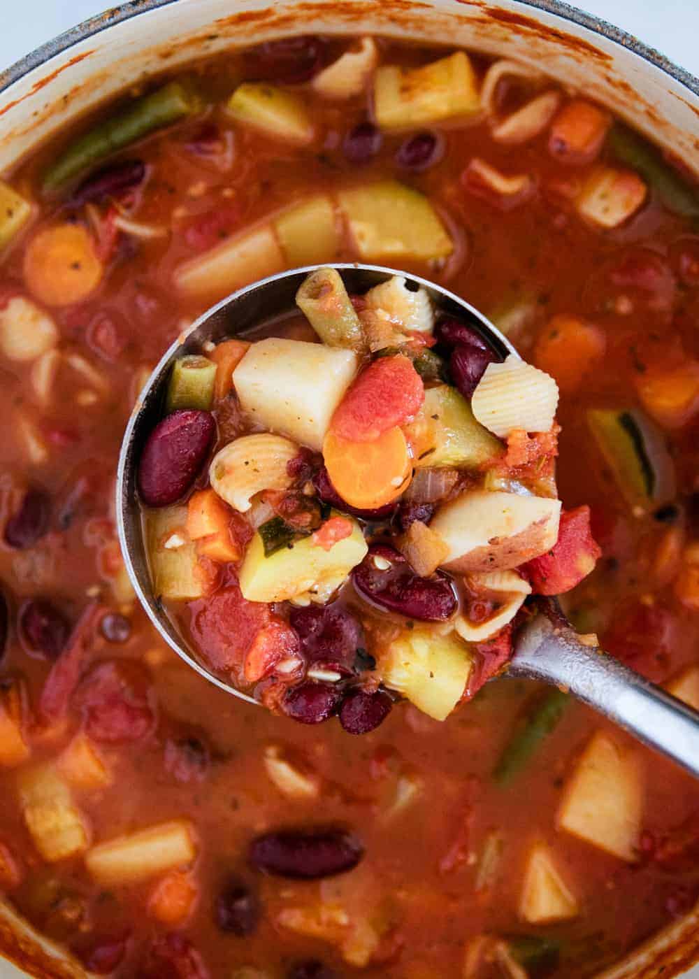 Scooping minestrone soup with a silver ladle.