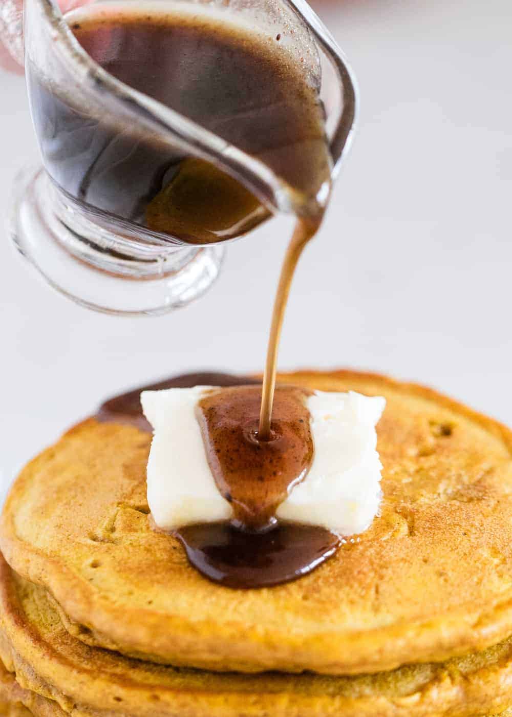 Pancake syrup being poured over pancakes.