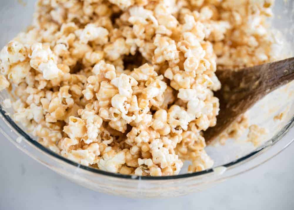 Mixing caramel corn in a glass bowl with a wooden spoon.