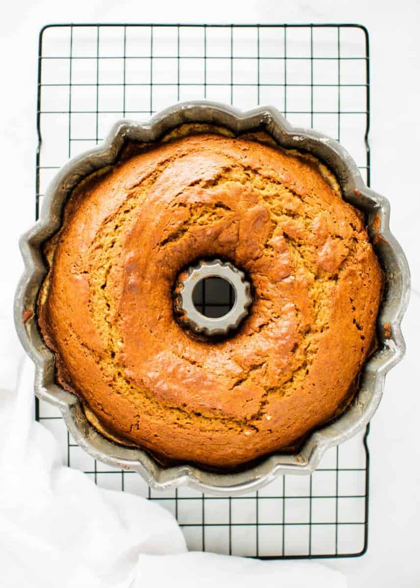 Soft and moist pumpkin bundt cake topped with a rich cream cheese frosting. This easy and delicious cake makes a great fall dessert! cooked pumpkin bundt cake in pan sitting on a baking rack