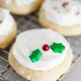 A close up of a frosted ricotta cookie with holly berry sprinkles