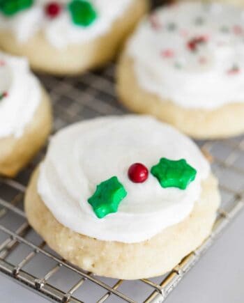 A close up of a frosted ricotta cookie with holly berry sprinkles