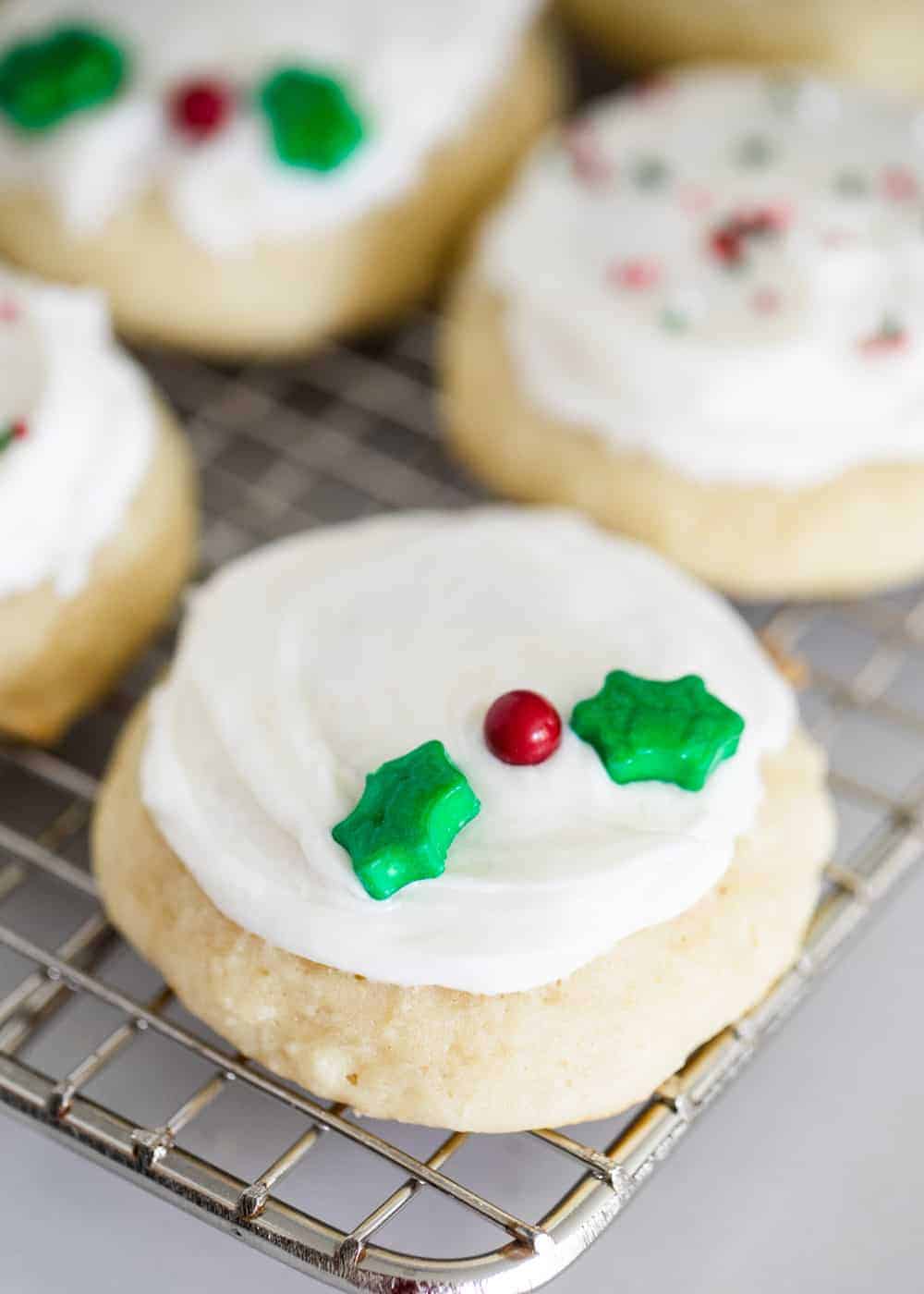 A close up of a frosted ricotta cookie with holly berry sprinkles 