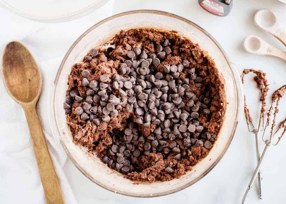 Chocolate and cookie dough in a glass bowl with a wooden spoon laying next to it. 