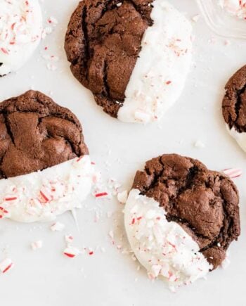 White chocolate dipped peppermint chocolate cookies set on a countertop with crushed candy canes.