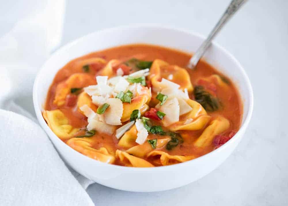 Bowl of tomato tortellini soup with fresh parmesan and basil.