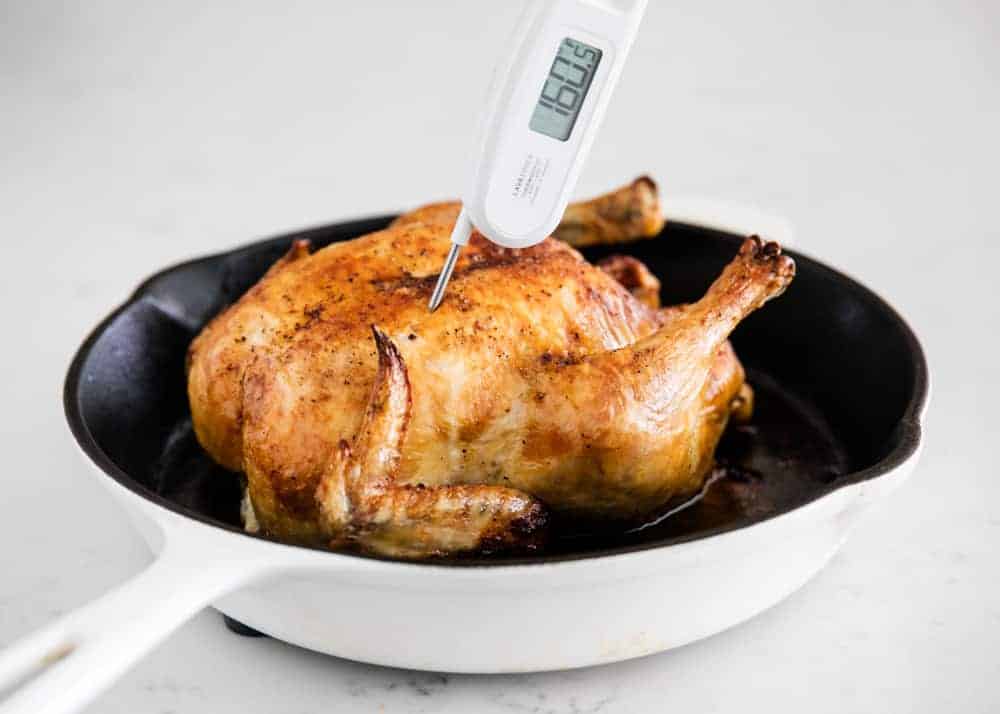 Roast chicken in a cast iron skillet with a meat thermometer in the breast.