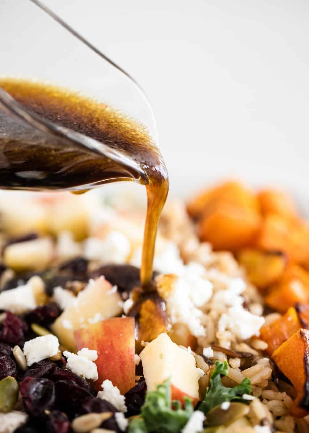 Pouring maple balsamic dressing on top of harvest salad.