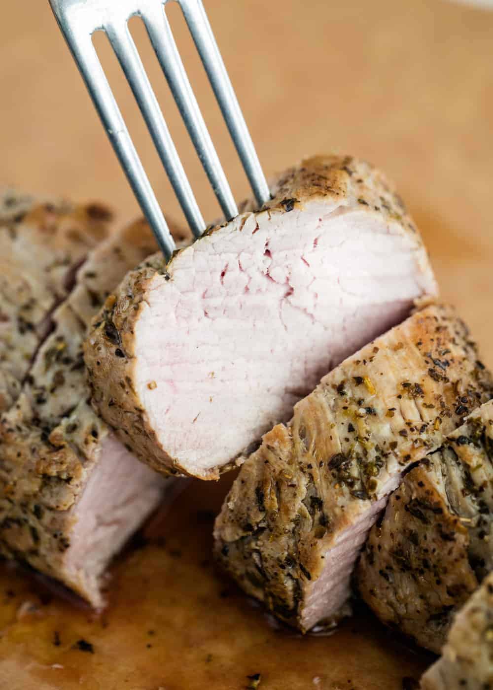 Fork sticking into a slice of pork tenderloin.