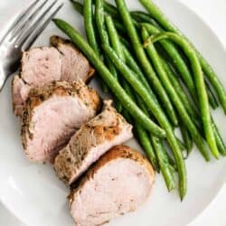 sliced pork tenderloin on a plate with green beans