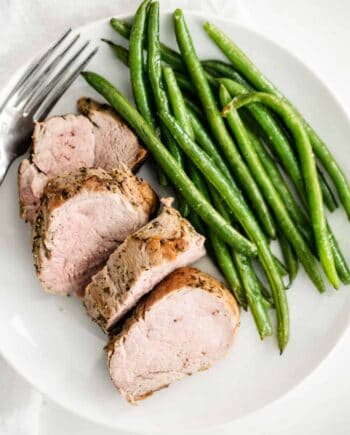 sliced pork tenderloin on a plate with green beans