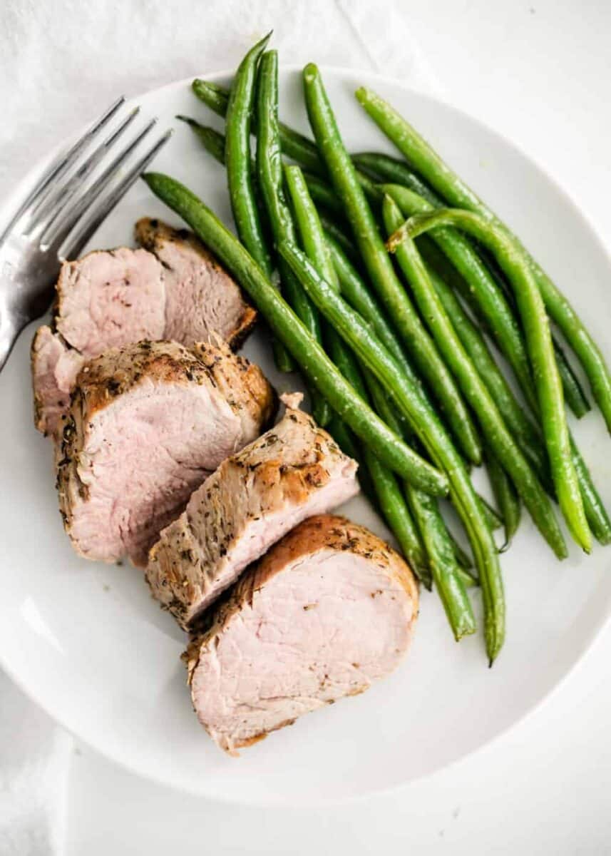 sliced pork tenderloin on a plate with green beans 