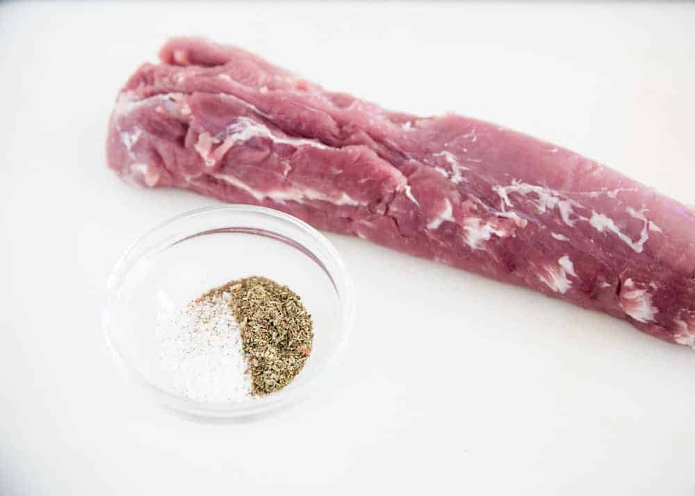 Seasoning the raw pork tenderloin with a spice rub.