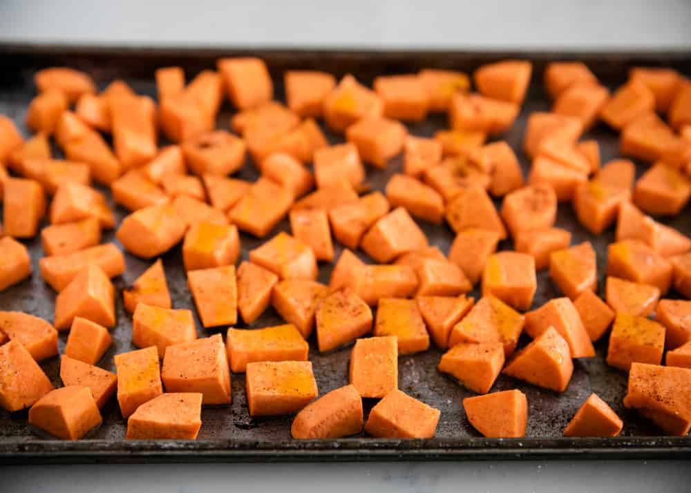 Seasoned roasted sweet potato cubes on a baking sheet.
