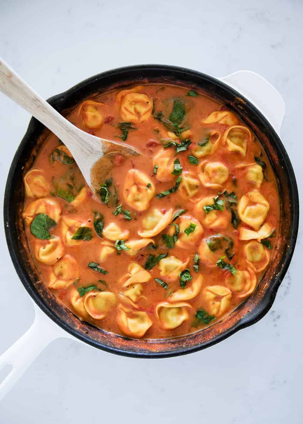 Creamy tomato tortellini soup in a skillet with a wooden spoon.