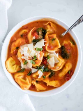 bowl of tomato tortellini soup with shaved parmesan on top