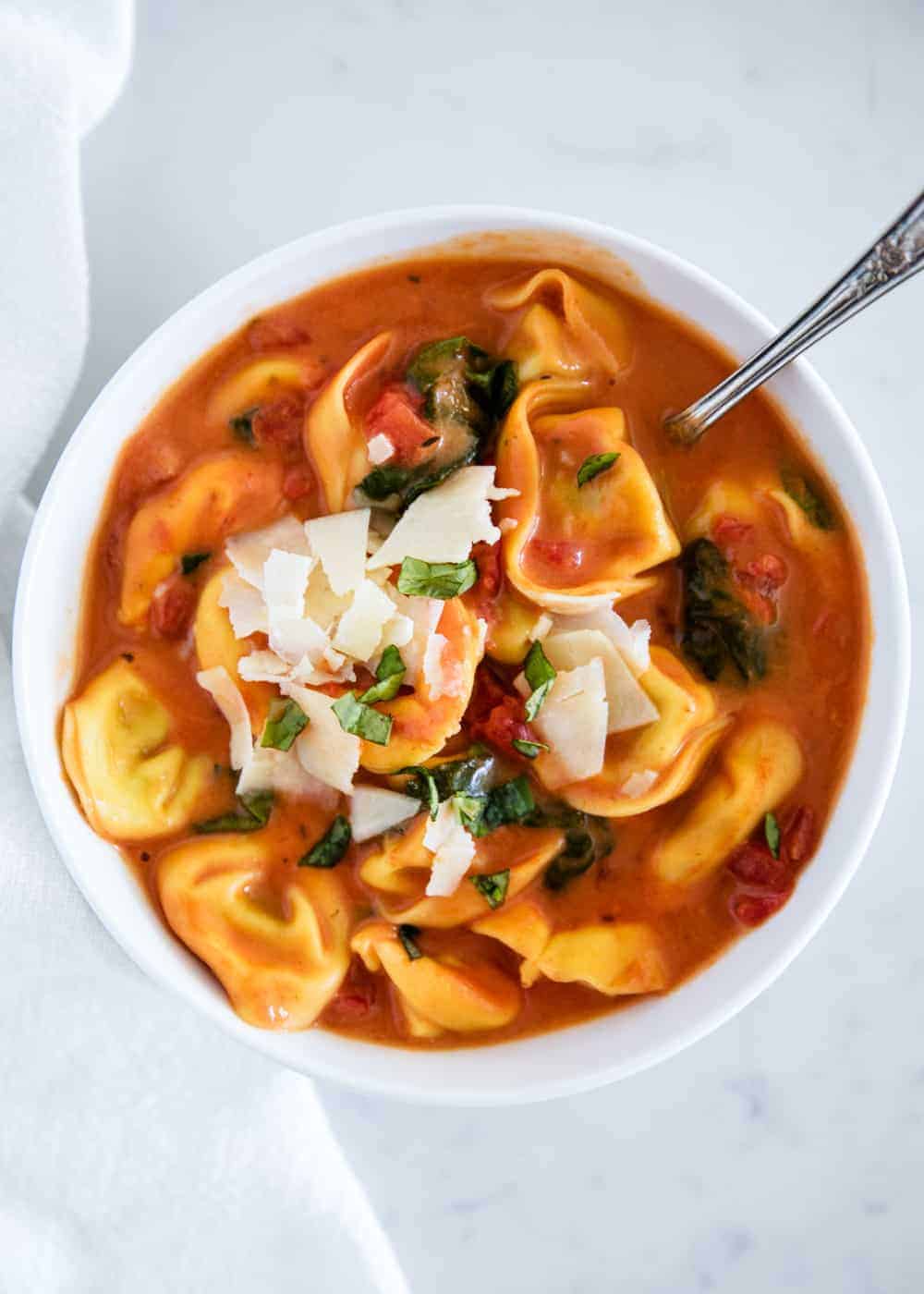 Bowl of tomato tortellini soup with shaved parmesan on top.
