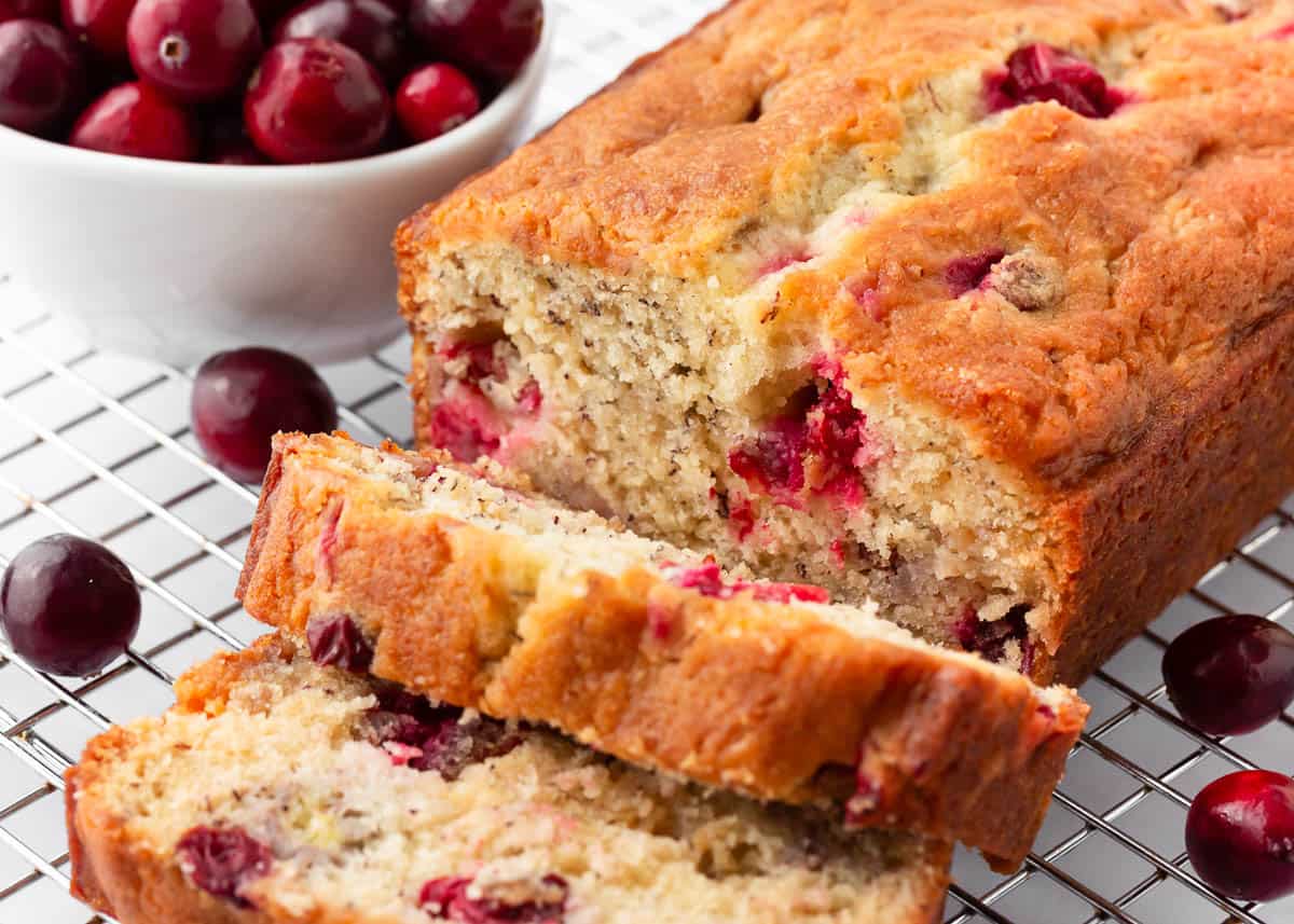 This moist and delicious cranberry banana bread is bursting with fresh, juicy cranberries and rich and creamy white chocolate chips in every bite! So soft and full of flavor. Sliced cranberry banana bread on a cooling rack.