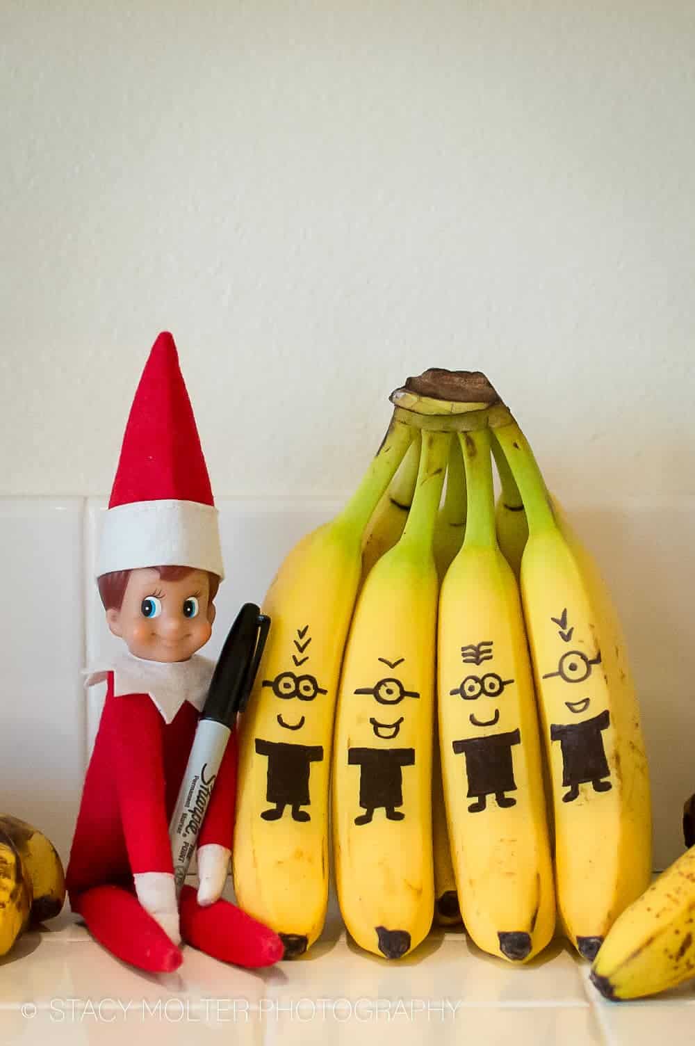 Elf on the shelf sitting by banana minions.