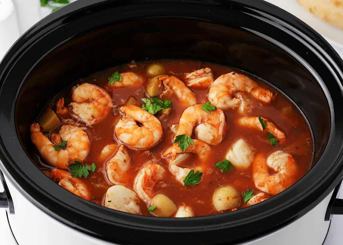 Seafood stew in a black slow cooker.