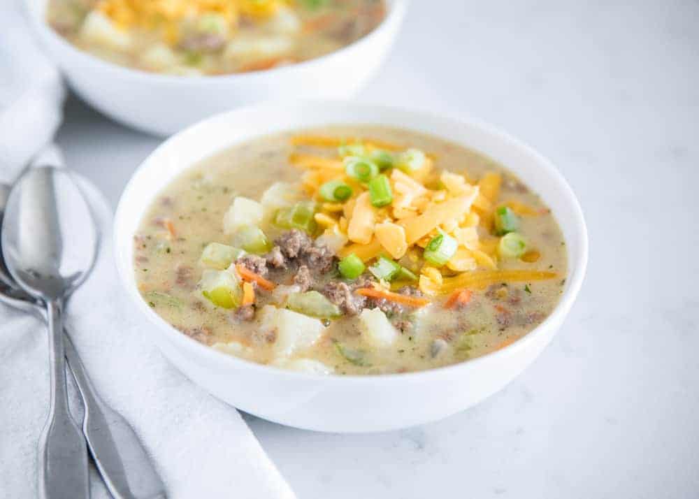 Cheeseburger soup in white bowl with cheese on top.
