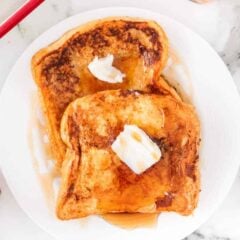 Eggnog French toast topped with melting butter and maple syrup, served on a white plate for a festive holiday breakfast.