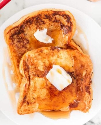 Eggnog French toast topped with melting butter and maple syrup, served on a white plate for a festive holiday breakfast.