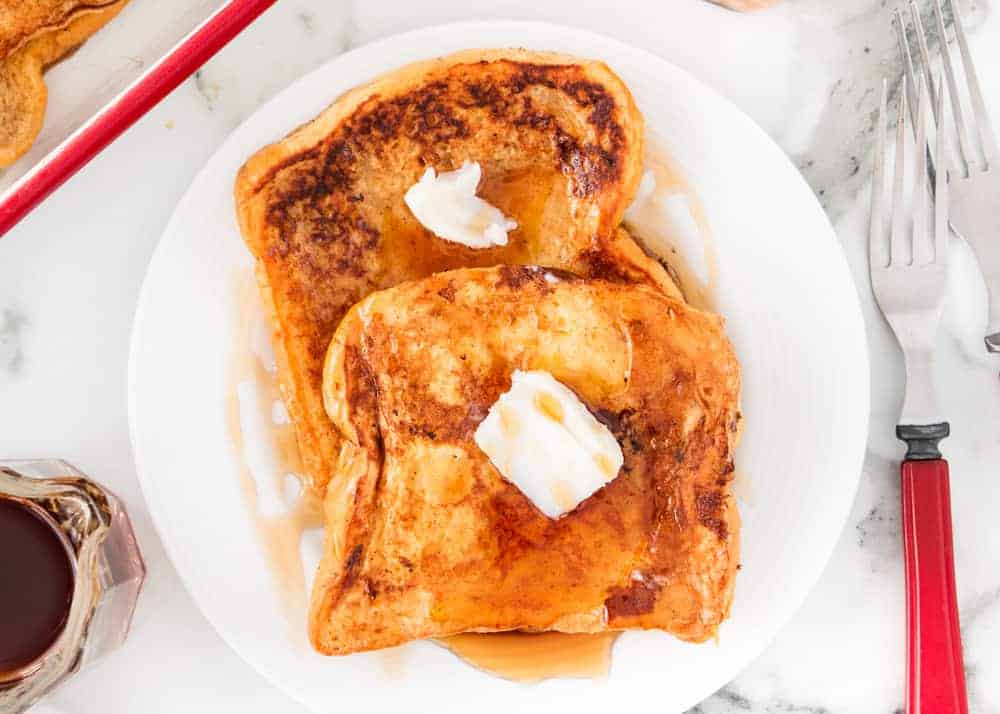 This easy eggnog french toast is the perfect recipe for your Christmas morning or holiday brunch! It's golden, rich and full of delicious eggnog flavor. Eggnog french toast topped with butter and syrup on a white plate.