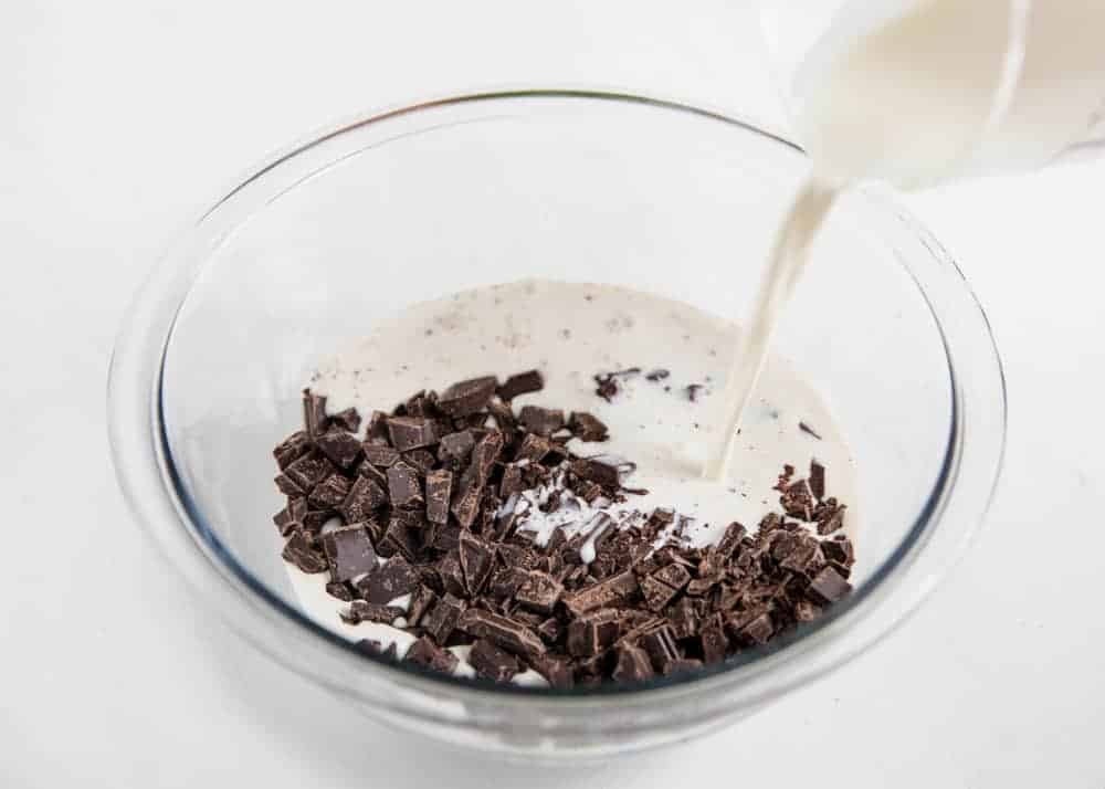 Pouring cream over chocolate in a glass bowl.