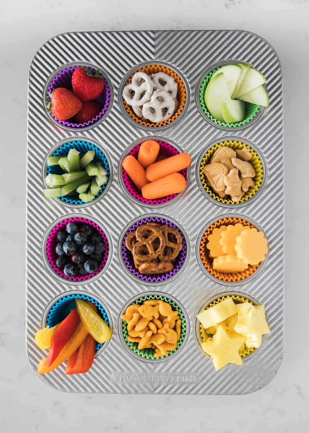 muffin tin filled with different types of snacks in each muffin cup 