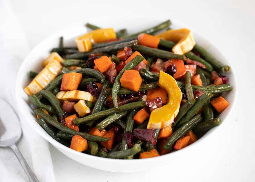 These maple roasted vegetables are sweetened with maple syrup and bacon for a crowd-pleasing side dish worthy of the holidays but easy enough for a weeknight meal! Maple roasted vegetables in white bowl.