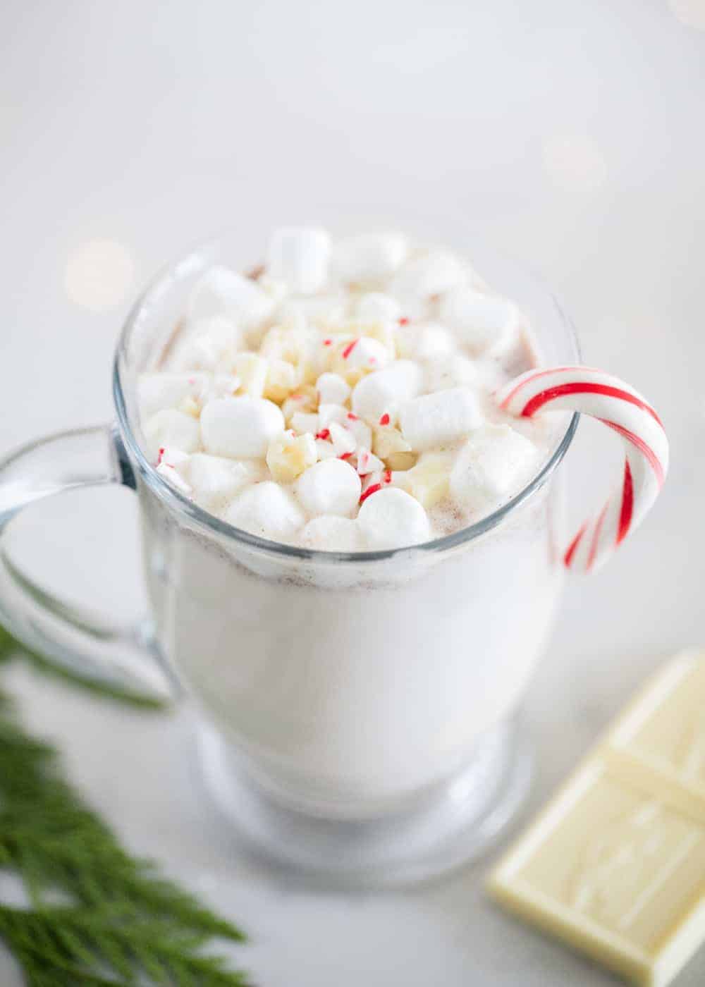 Snickerdoodle hot chocolate in a glass mug with mini marshmallows and a candy cane.