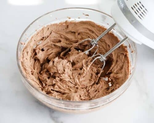 mixing chocolate buttercream frosting in glass bowl