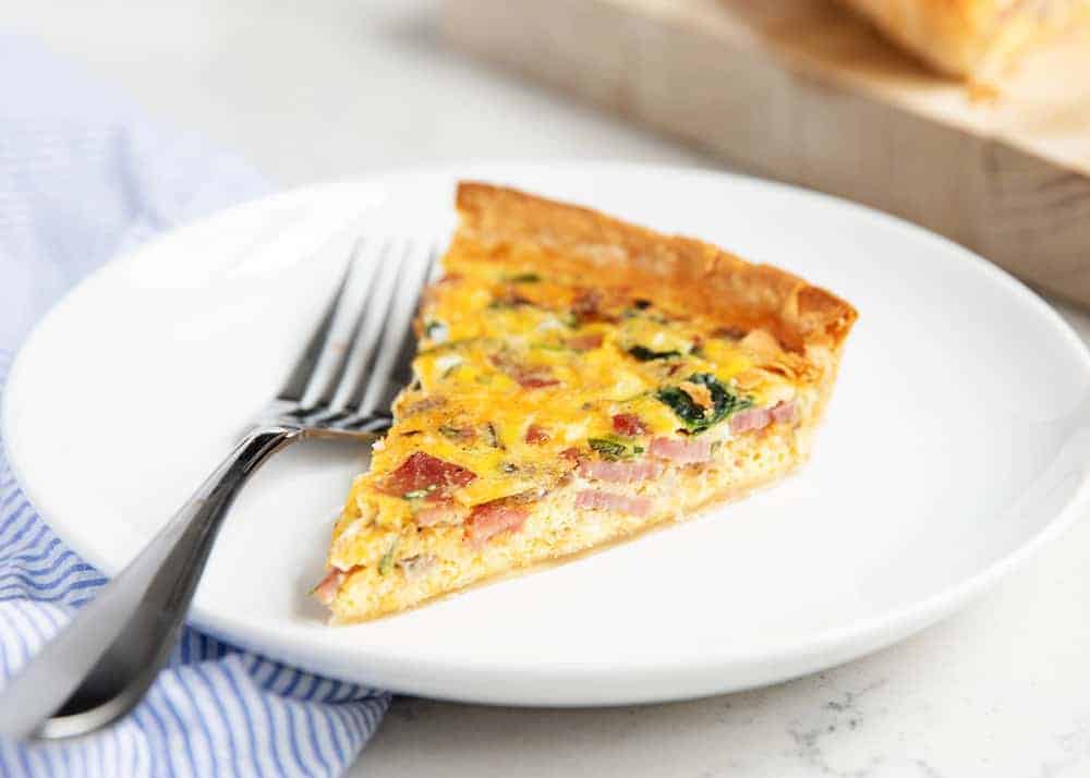 Slice of ham and cheese quiche on a white plate.