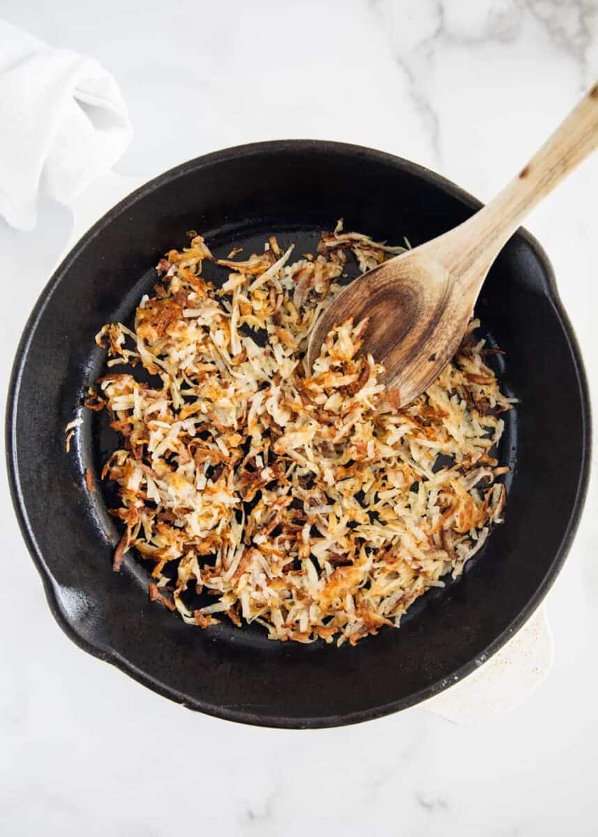 cooking hash browns in skillet with wooden spoon 