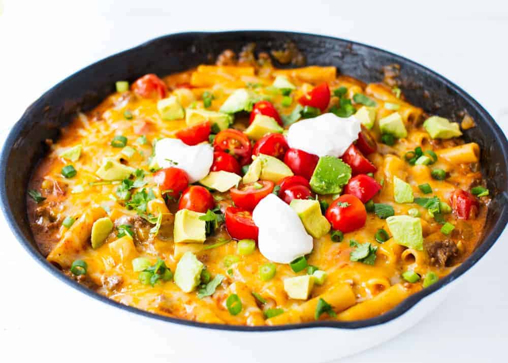 This ONE POT cheesy enchilada pasta recipe is so simple and completely delicious. It's done in 30 minutes from start to finish and is a family favorite! Enchilada pasta in a cast iron skillet.