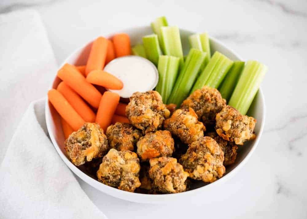 Sausage balls in a white bowl with vegetables.