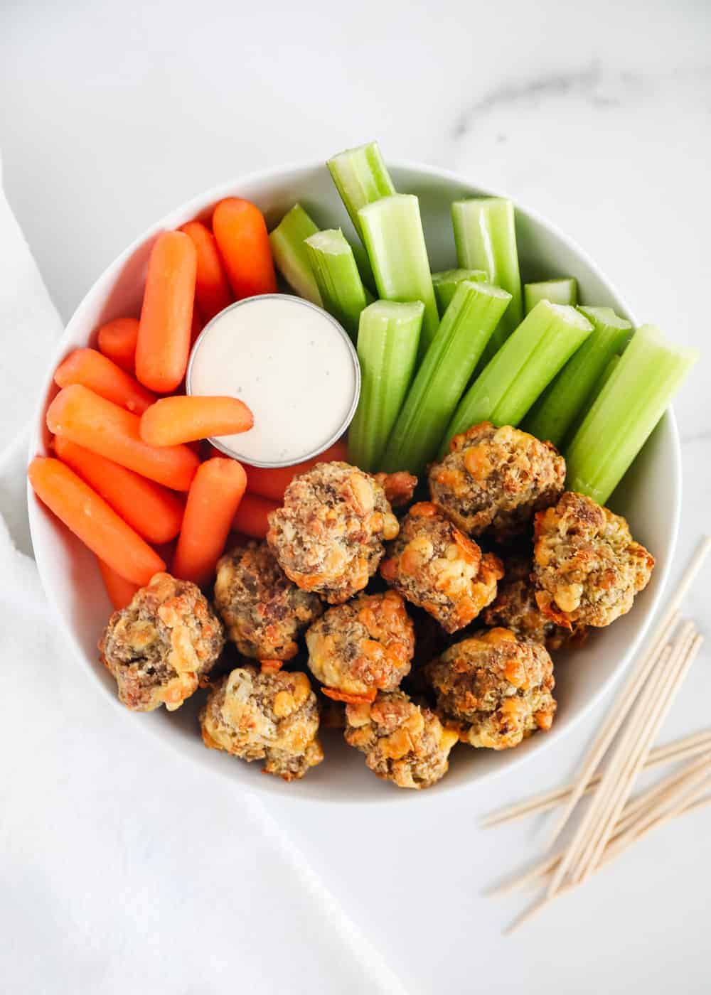 Sausage balls in a white bowl with vegetables.