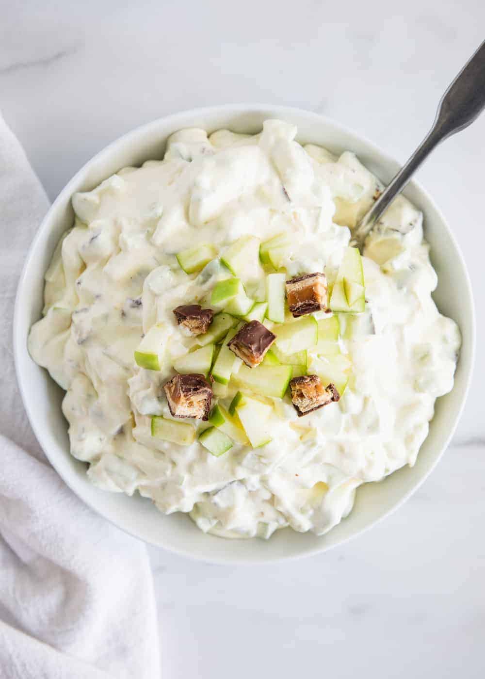 Snicker apple salad in white bowl with spoon.