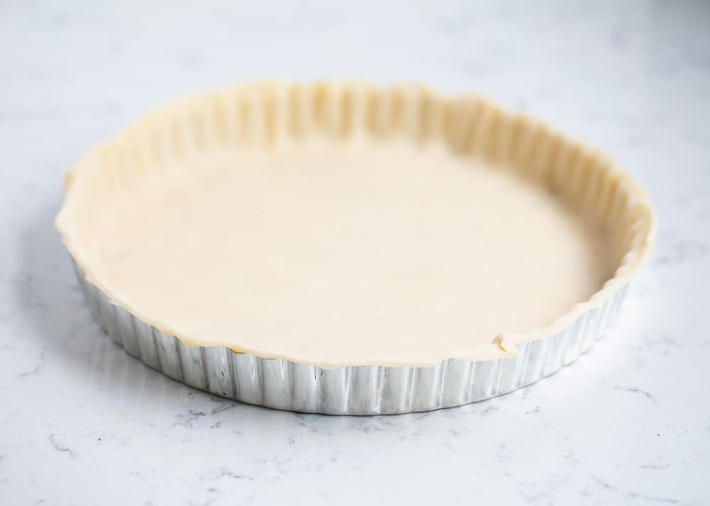 Pie dough is pressed in a tart pan.