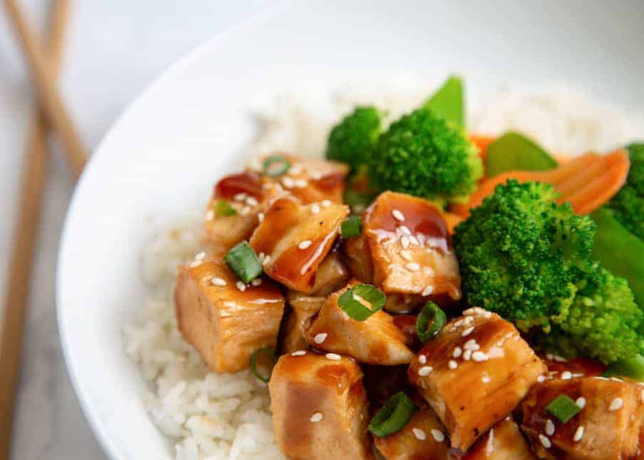 Close-up of teriyaki chicken in a bowl with rice and veggies.