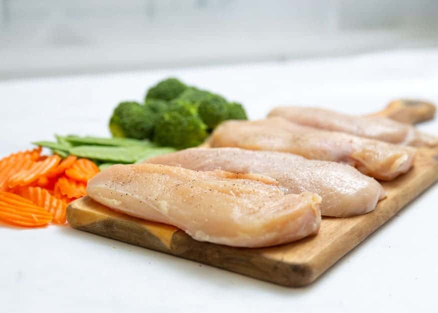 Raw chicken breasts on a cutting board.