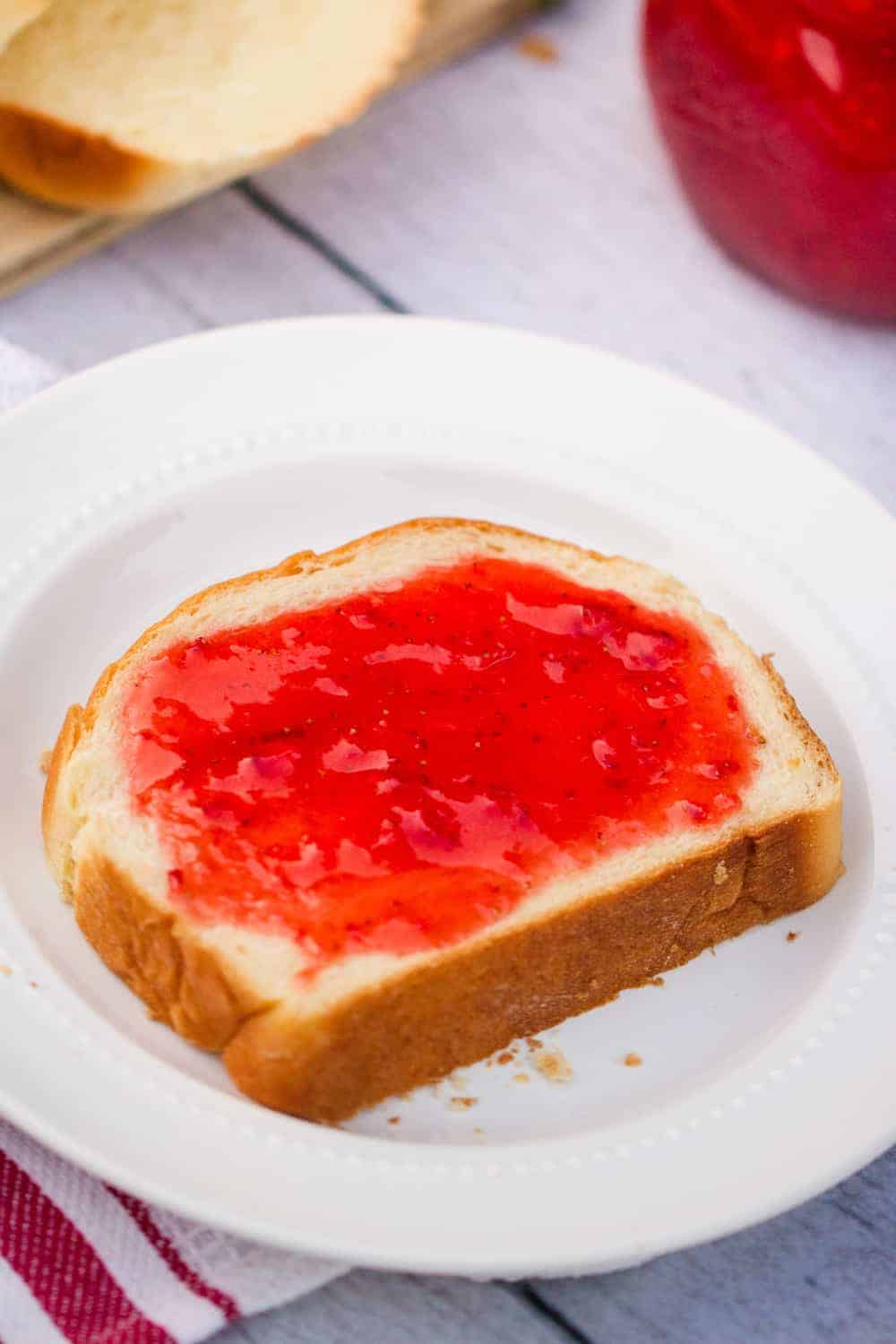 snede van zelfgebakken brood op een wit bord met aardbeienjam erop 