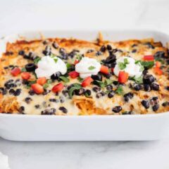 Easy chicken enchilada casserole in white baking dish garnished with cheese, sour cream and tomatoes.