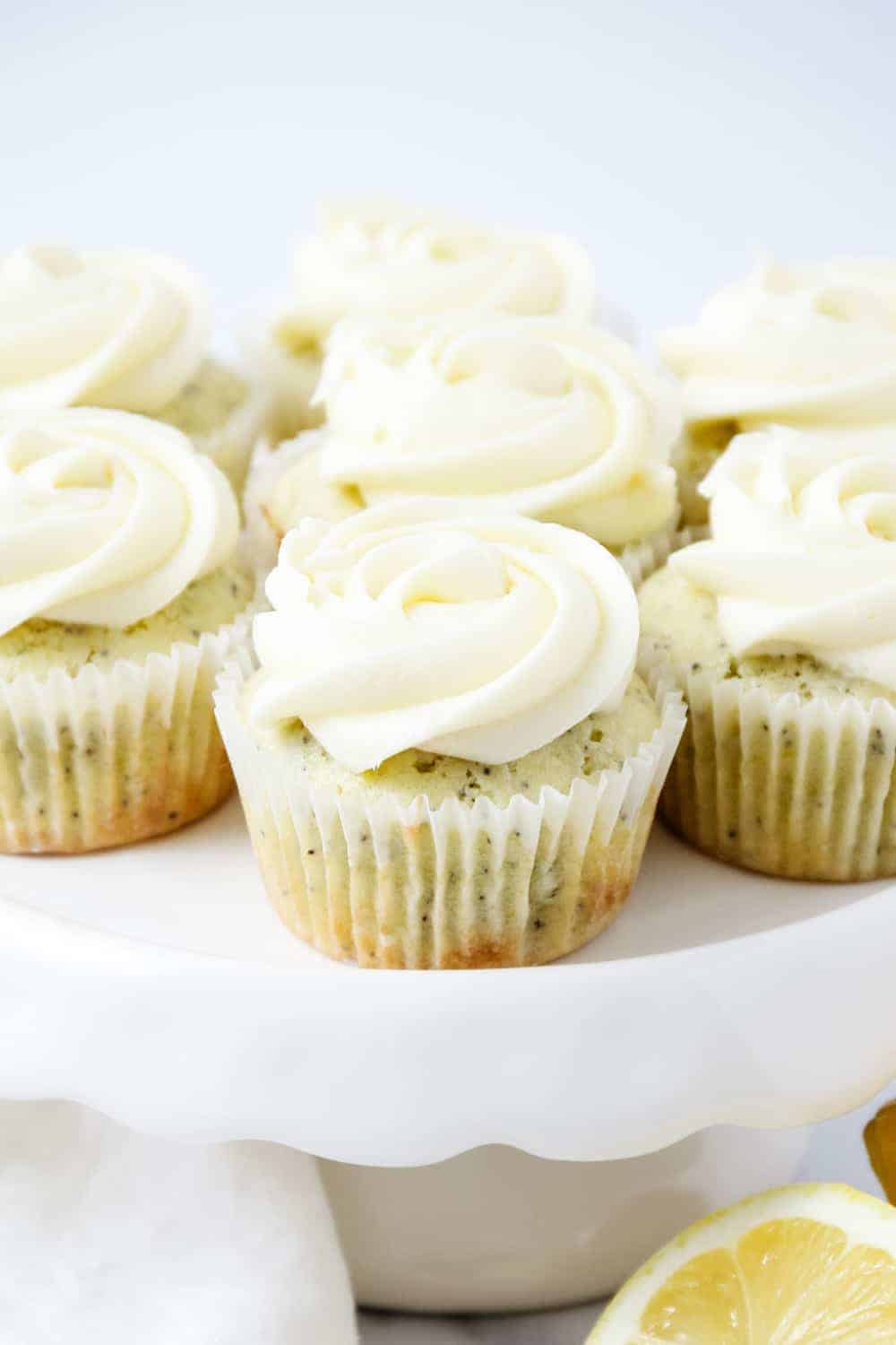 Frosted lemon poppy seed cupcakes on a white cake stand.