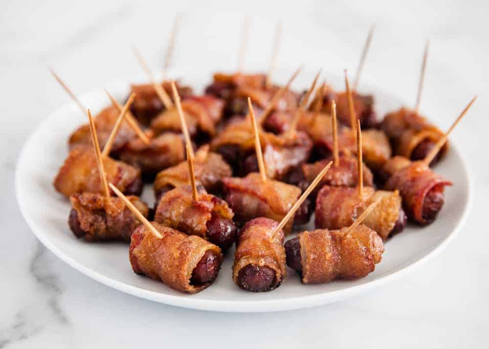 Bacon wrapped little smokies on white plate.