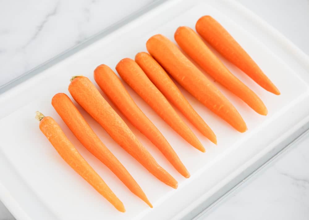 Peeled whole carrots on a cutting board.