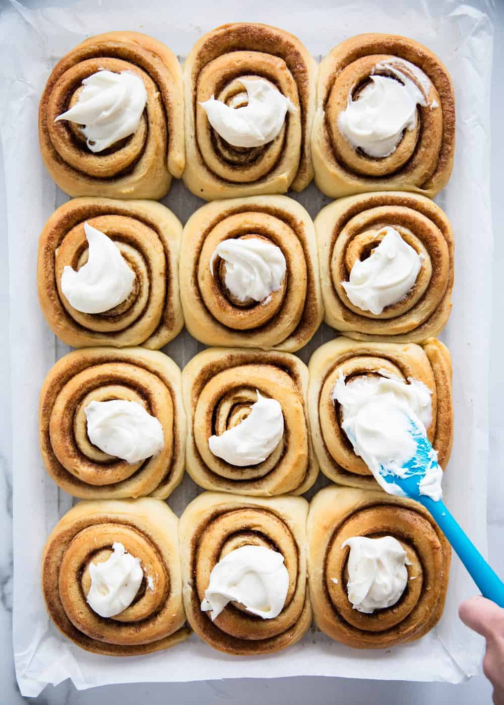 Frosting cinnamon rolls with a spatula.