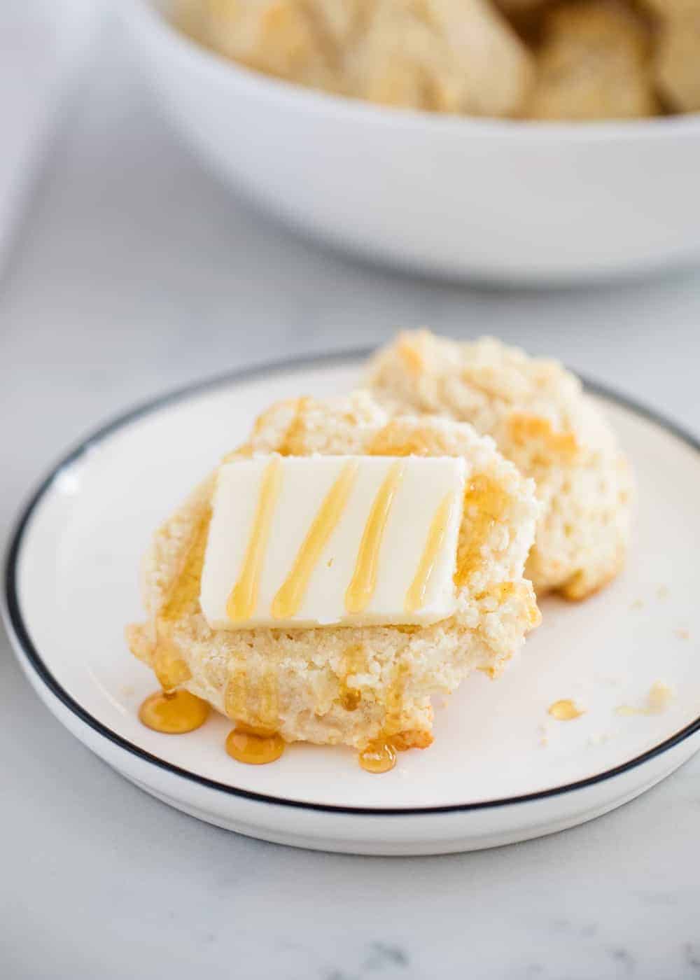 Biscuit with butter and honey on white plate.